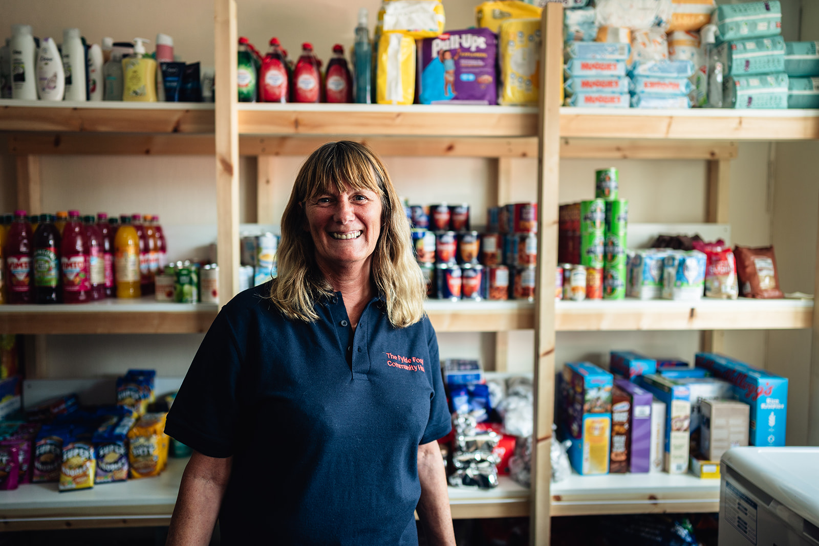shows employee at the Fylde community hub, in front or stocked shelves 