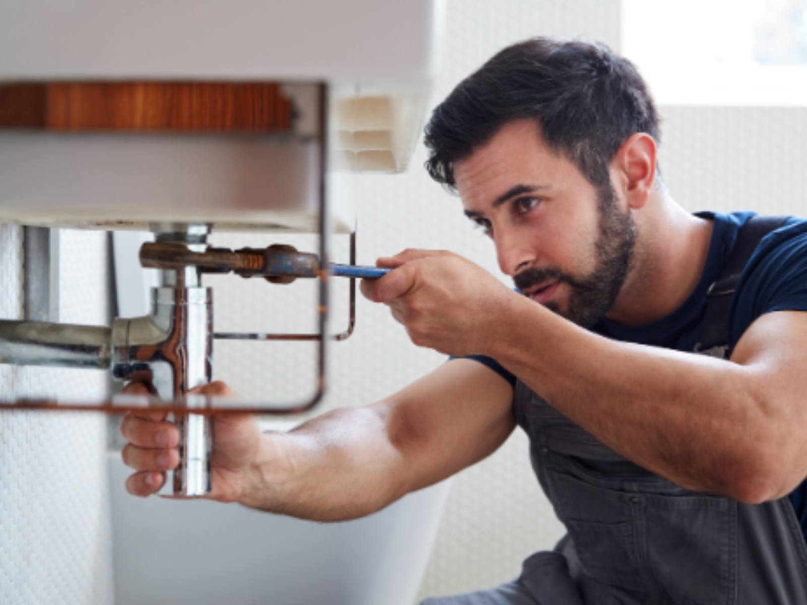 Man tightening a pipe under a bathroom sink smiling