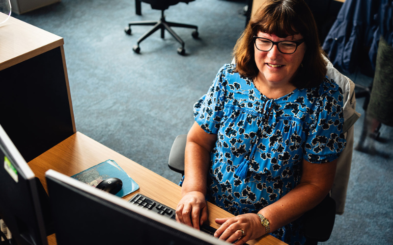 Brown haired lady sitting at her desk smiling