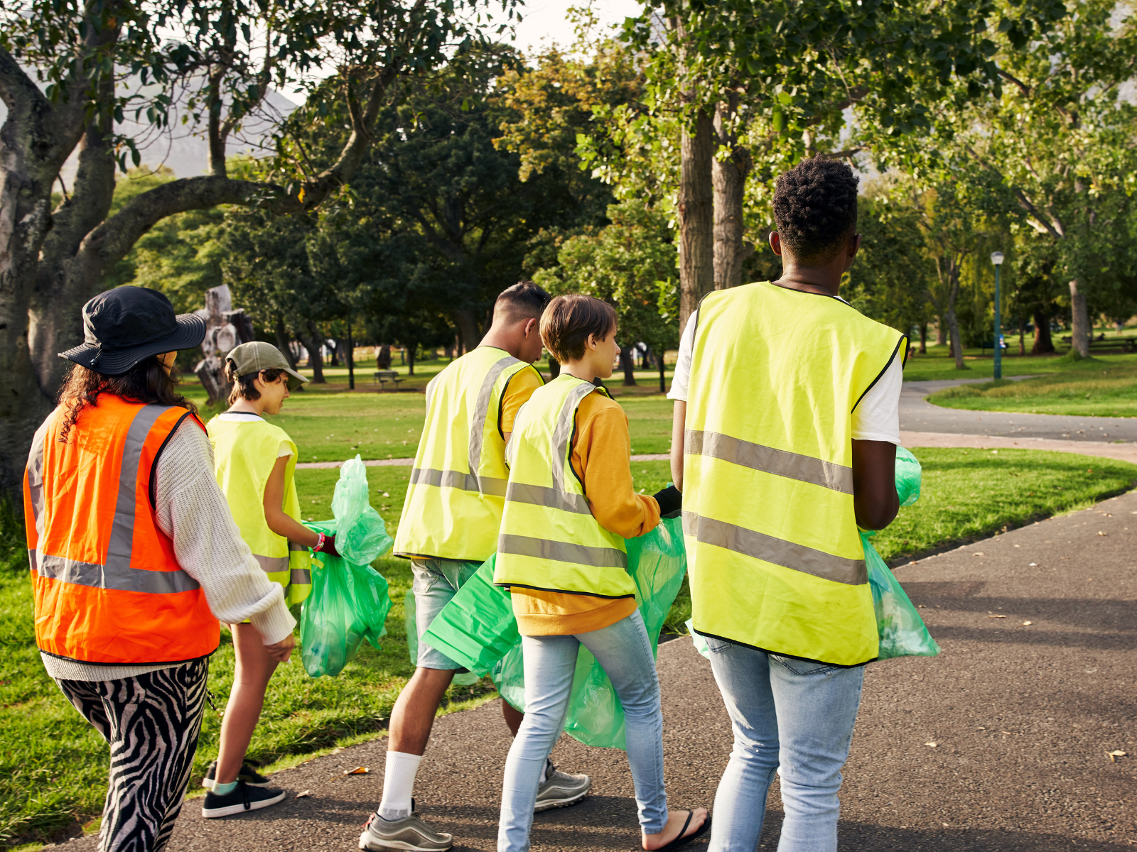 Group of people in yellow and orange vests walking with rubbish in bags 